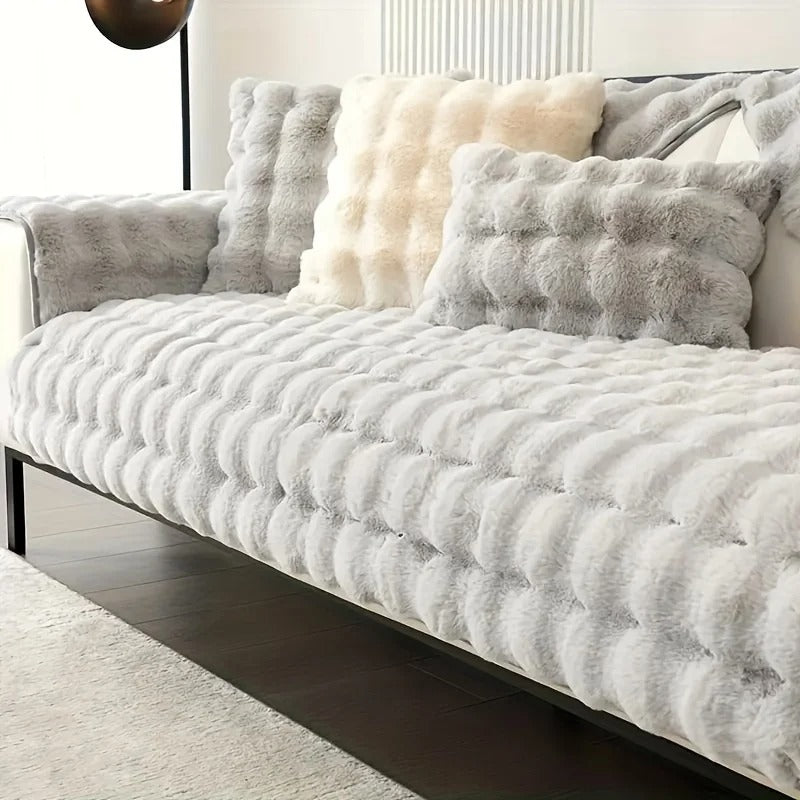 Een luxe moderne bank bekleed met een zachte, witte Wagner met golvende textuur - Fluffy Bankhoes Universeel van Act Design Shop en versierd met verschillende donzige kussens in de kleuren wit en beige.