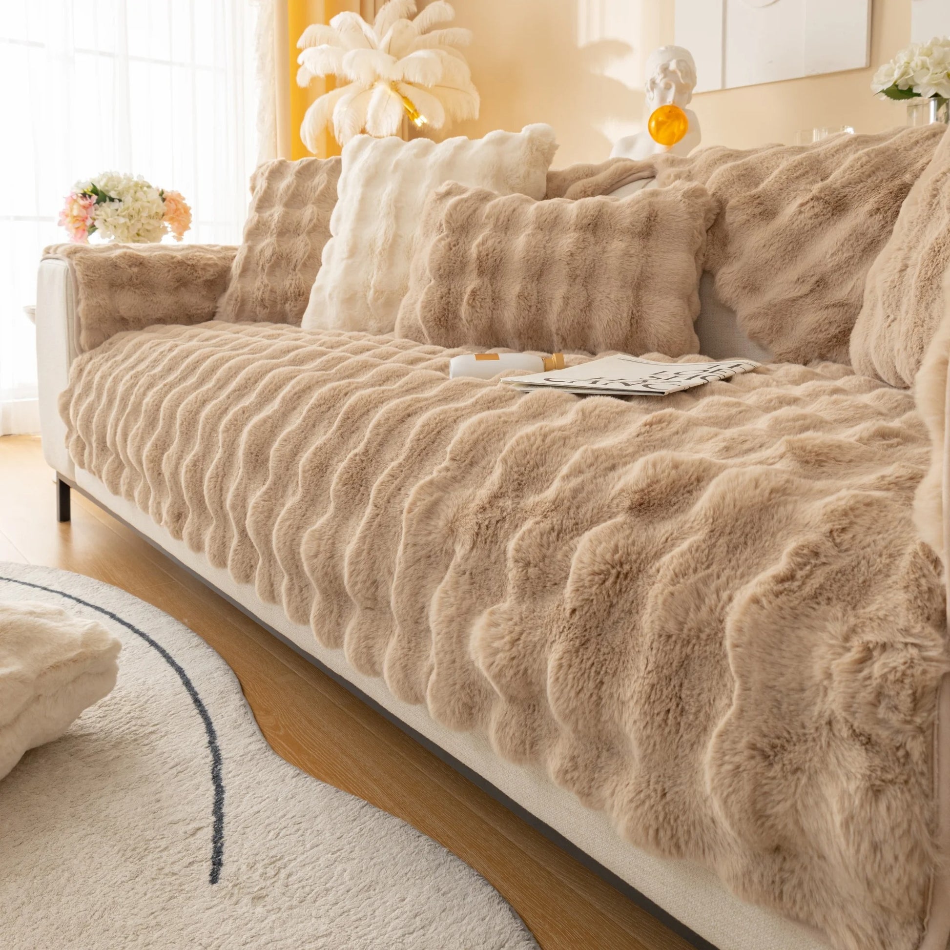 Een gezellige woonkamer met een luxe bank bekleed met een pluche, beige Act Design Shop Wagner - Fluffy Bankhoes Universeel. De kamer baadt in warm licht, wat de uitnodigende en comfortabele sfeer versterkt.